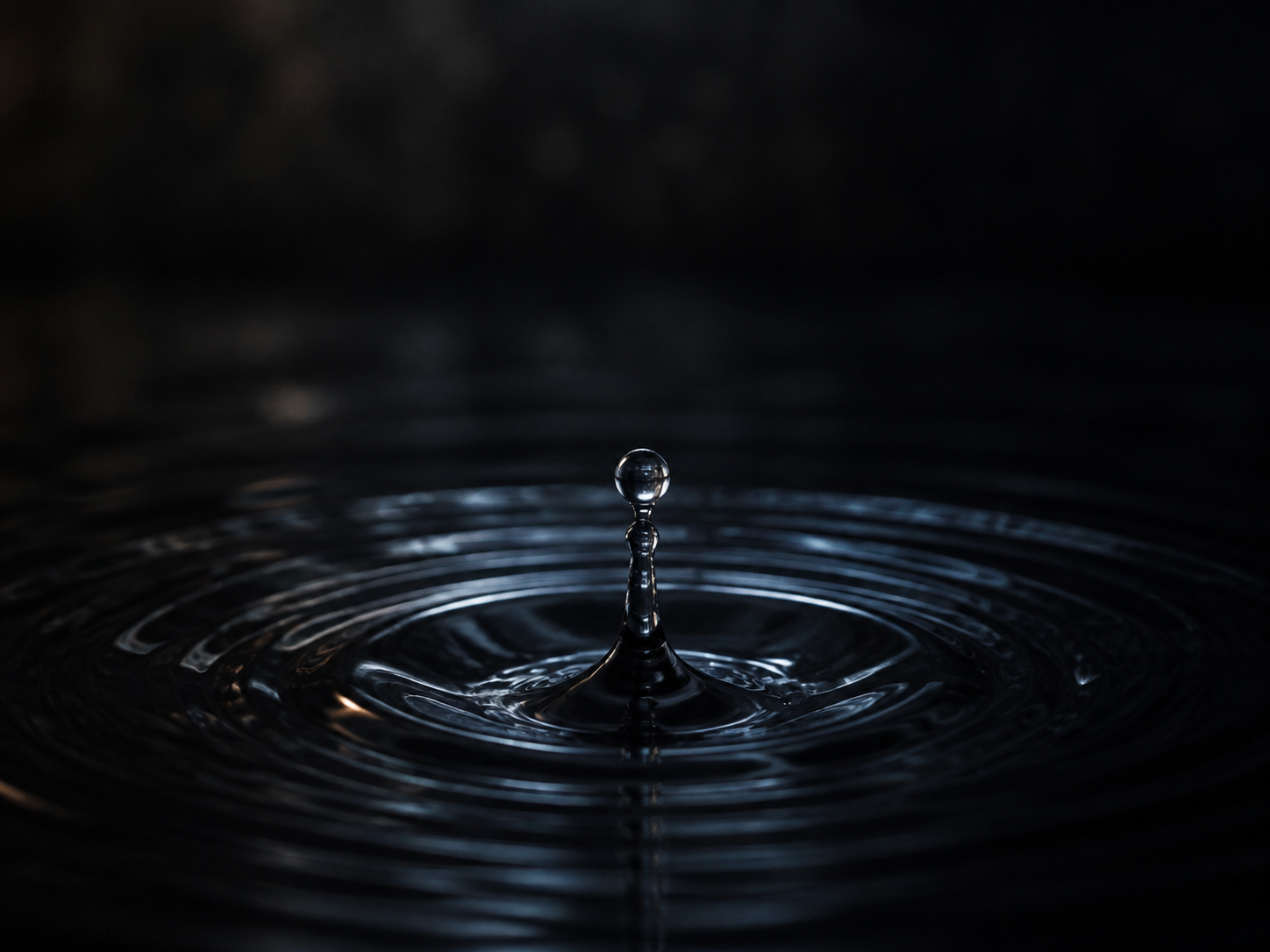 A single drop rising from dark rippling water